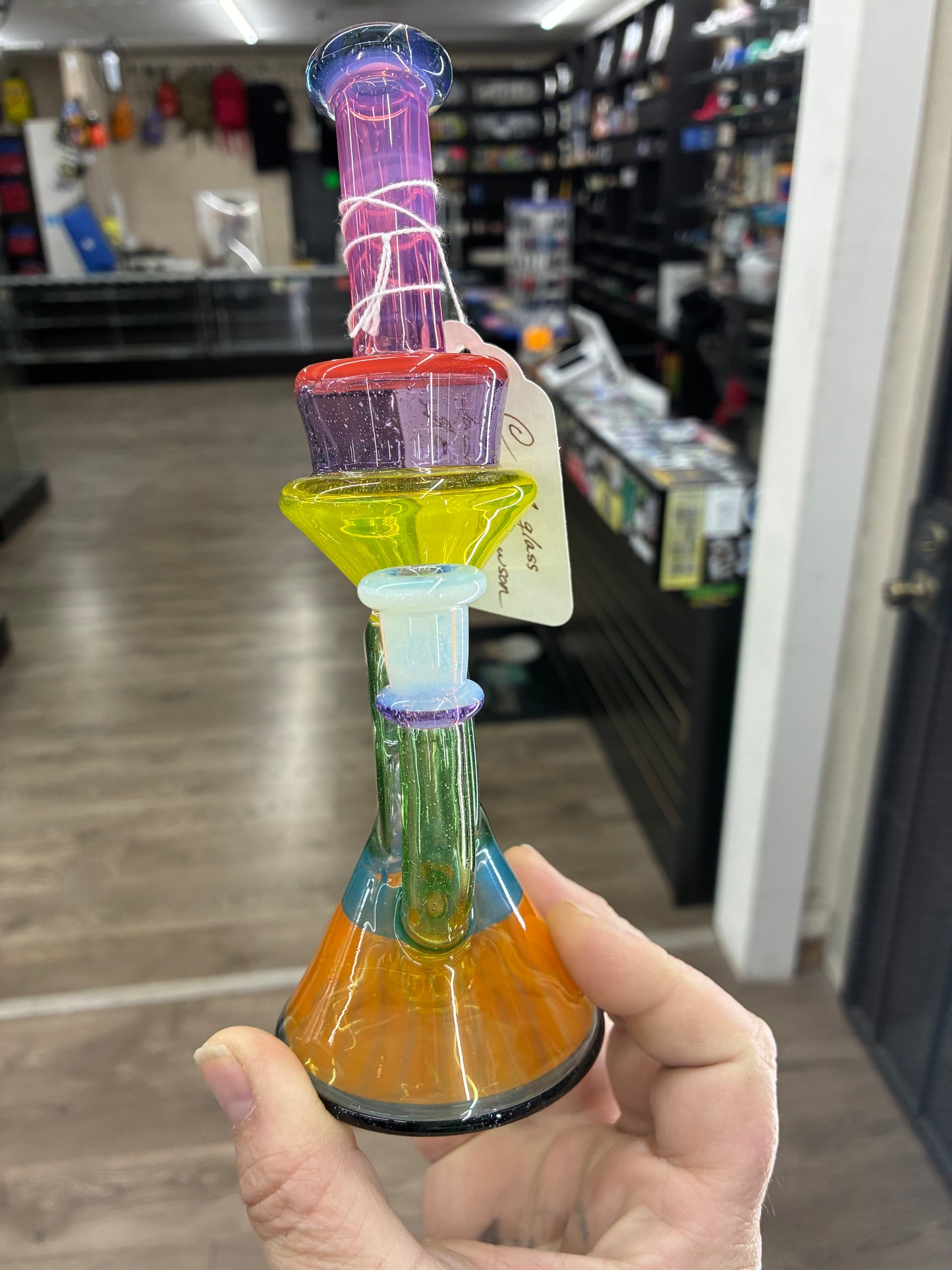 Colorful glass smoking accessory held in a hand with a store interior in the background